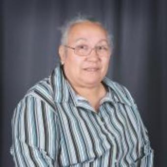 Photo of Betty Mitchel, blue-gray-black-white stripe-patterned collared long-sleeved shirt, rectangle-framed glasses, hair styled up, smiling.