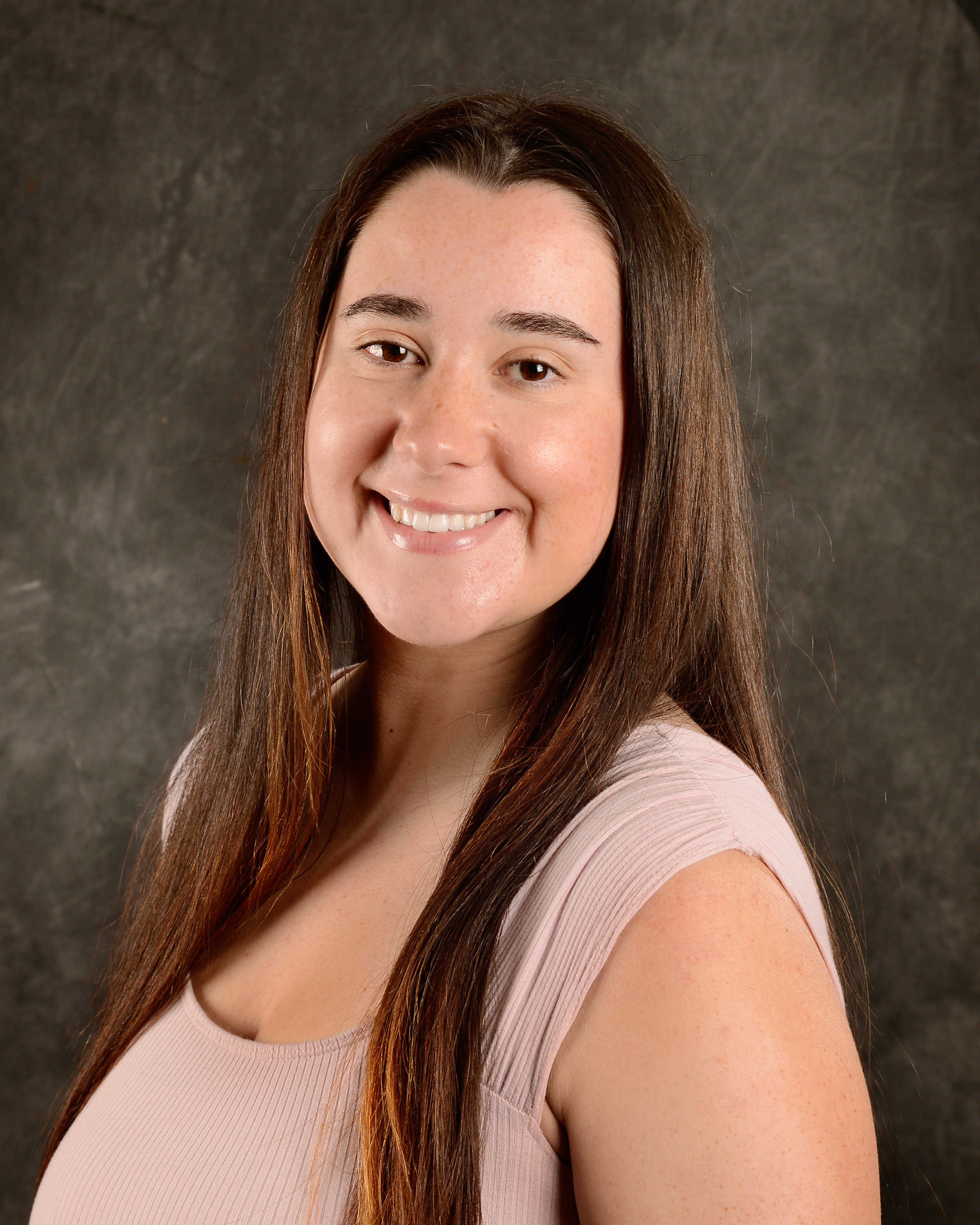 Photo of Bryana Leapley-Priest, long brown hair styled down, crepe short-sleeved shirt, smiling.