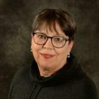 Photo of Ildiko Melis, short brown hair, rounded black frame glasses, earrings, smiling.