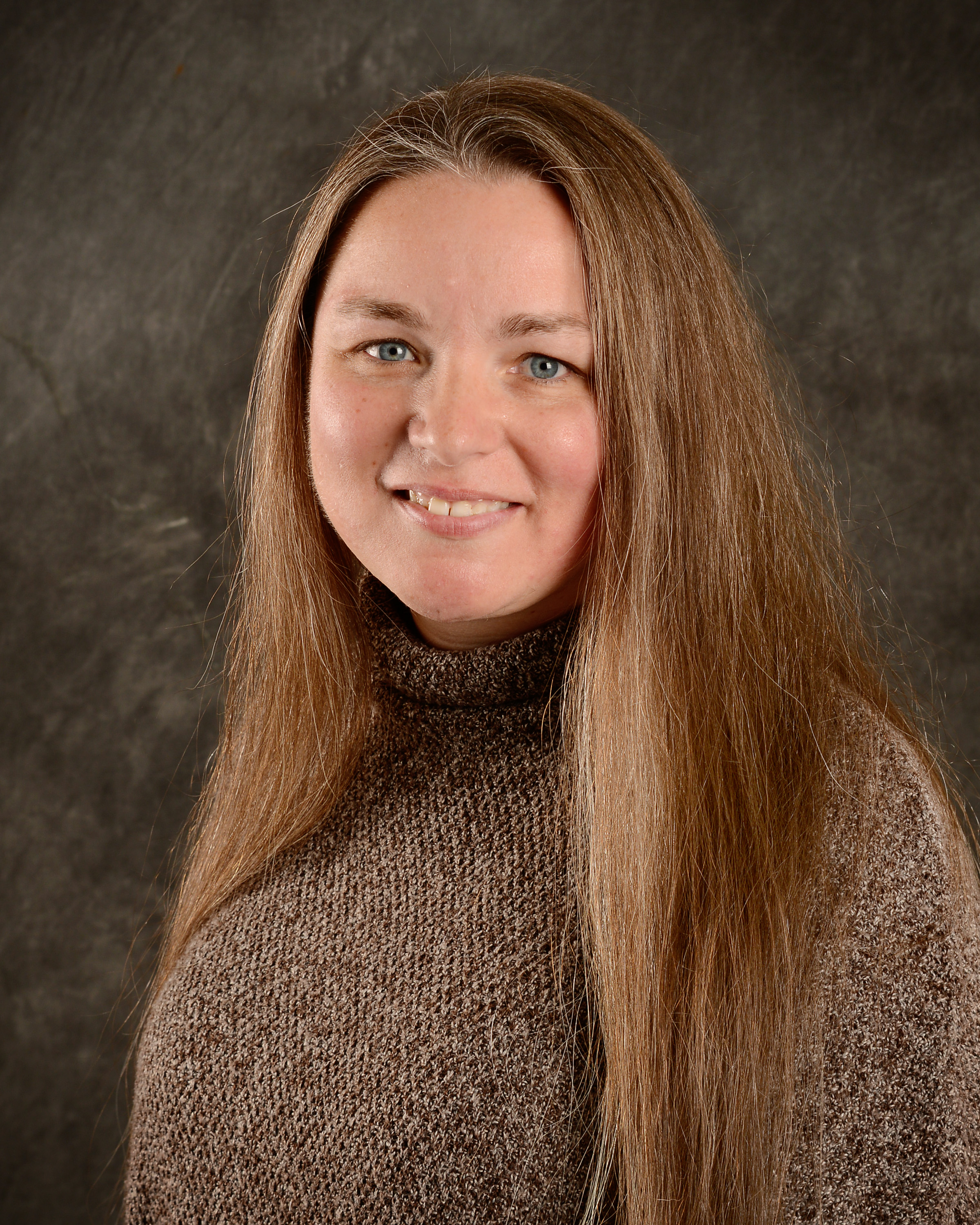 Photo of Brandy Ball, dark beige turtle-neck sweater, long light brown hair styled down, smiling.