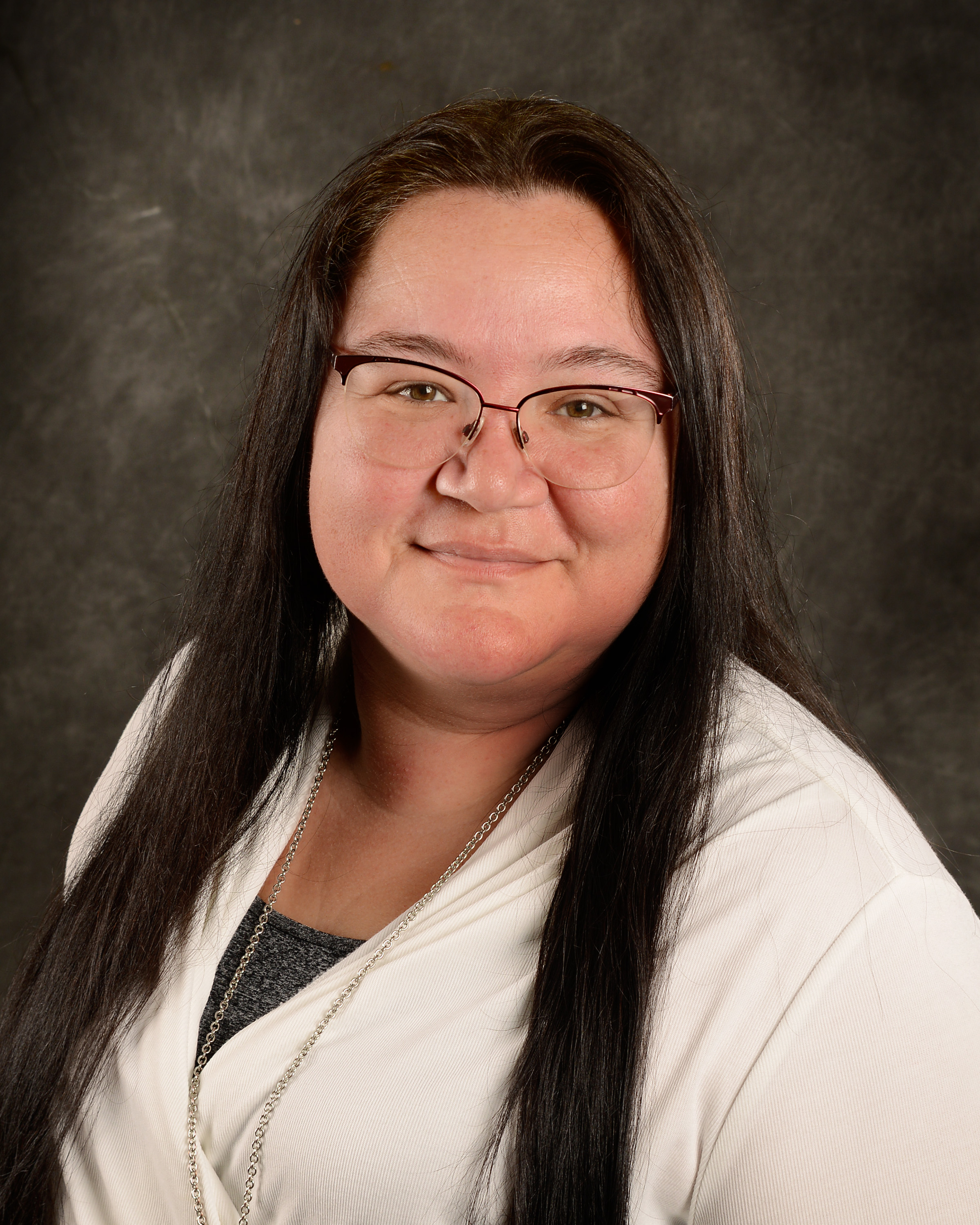 Photo of Brenda Clor, gray and white blouse, long dark brown hair styled down, browline glasses, with a subtle smile.